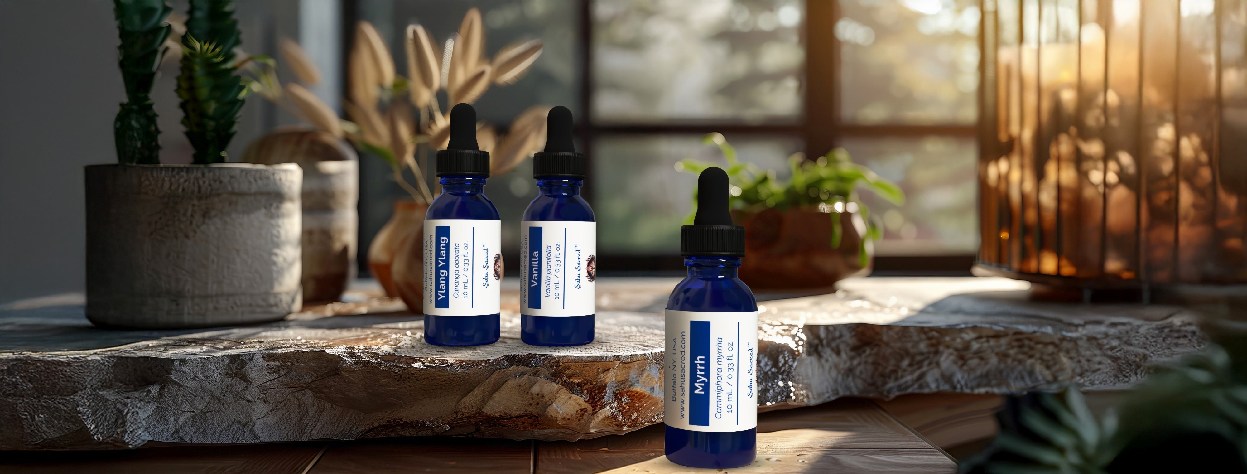 Blue Sahu Sacred Oils bottles of Ylang Ylang, Vanilla, and Myrrh placed on a wooden surface with soft natural light in the background.