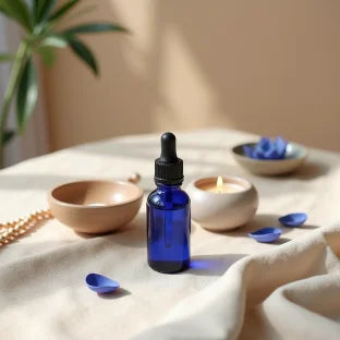 Blue glass dropper bottle on a light fabric surface with candles and bowls in the background