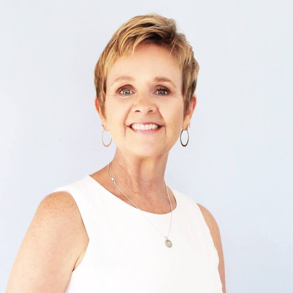 Woman with short blonde hair wearing a white sleeveless top against a light blue background