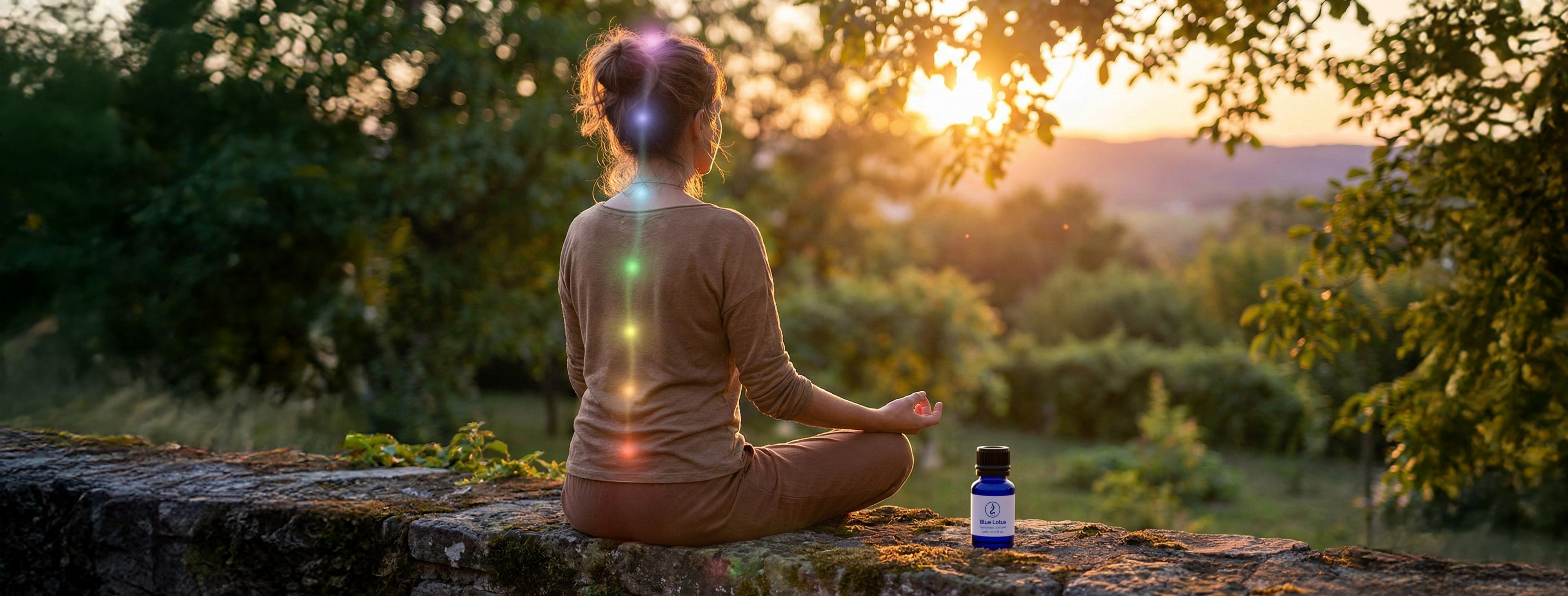 Person meditating at sunset with glowing chakras and a blue lotus oil bottle beside them.