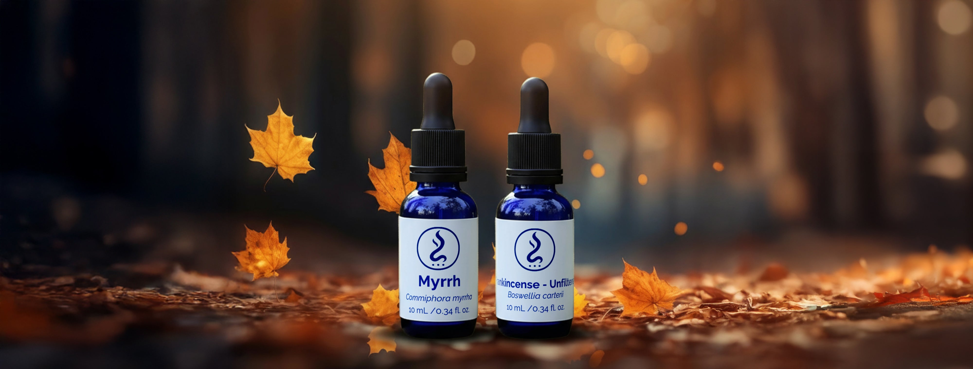 Two blue glass bottles of Sahu Sacred Oils Myrrh and Frankincense placed on autumn leaves with a warm blurred forest background.